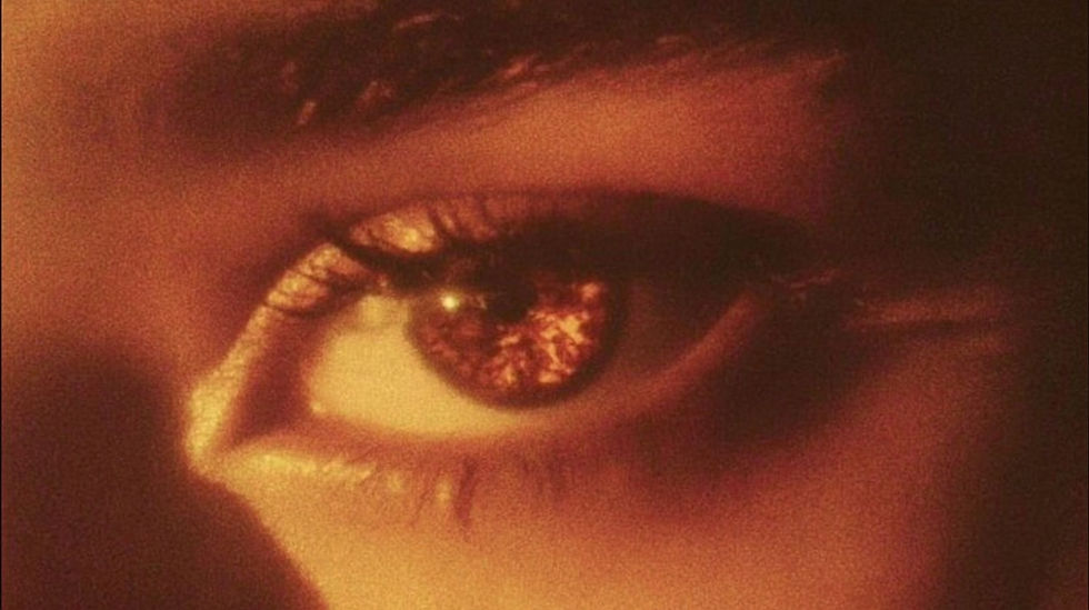 Close-up of a human eye in warm, golden-red lighting with a glowing reflection, creating a dramatic and artistic mood.