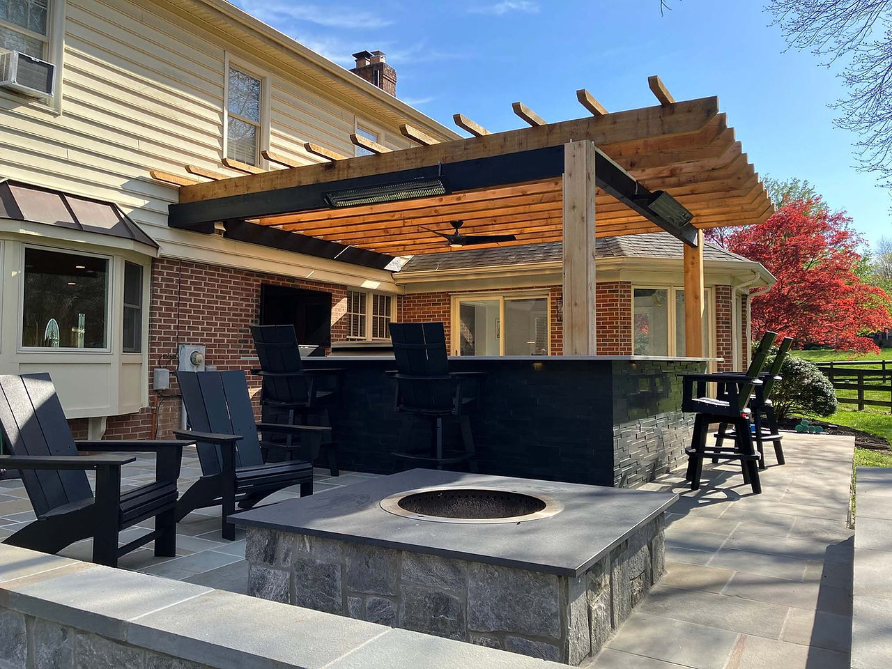 Pergolas:  A light wood, modern pergola on top of a black stone bar. The pergola and bar is set behind a modern stone fireplace