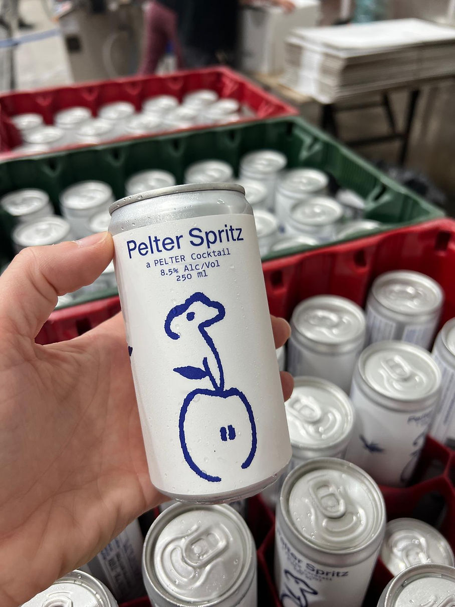 Hand holding a “Paller Spritz” can in front of a crate of similar cans