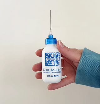 a hand holding a small bottle of sewing glue