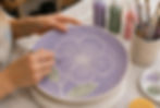 Diseño floral mediante la técnica de esgrafiado en plato lila durante una sesión de pintura libre.