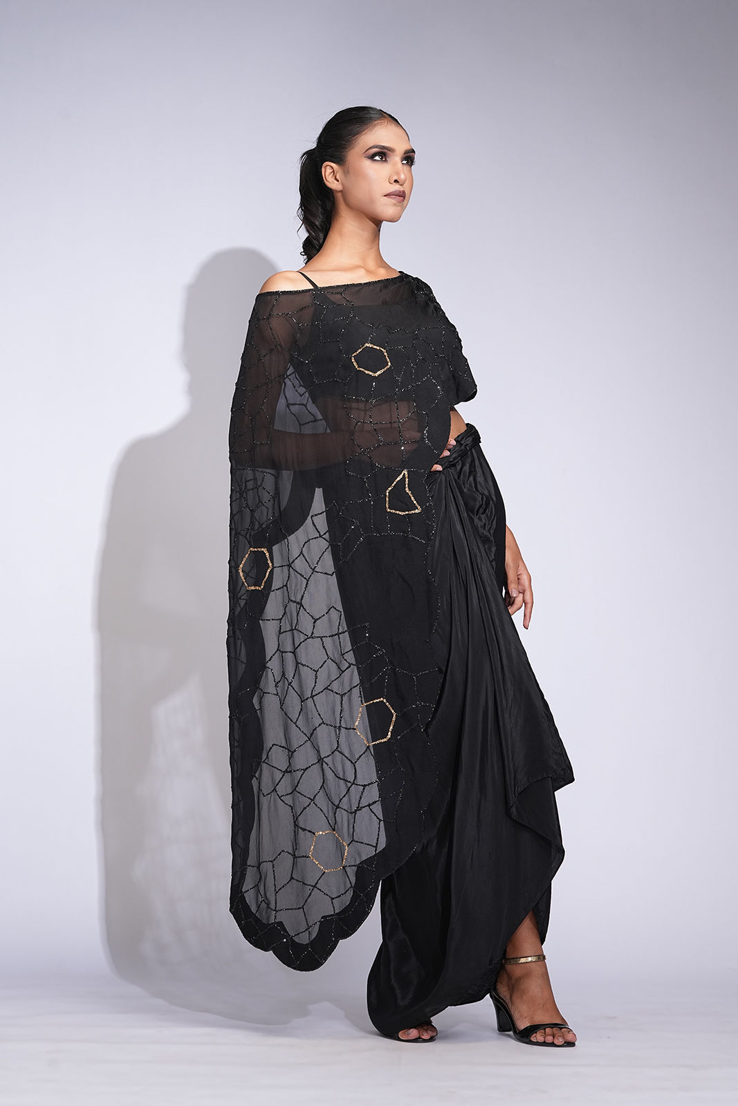 Model wearing black crepe dhoti-style draped skirt paired with a gold sequin embroidered organza cape by SHRUTI S