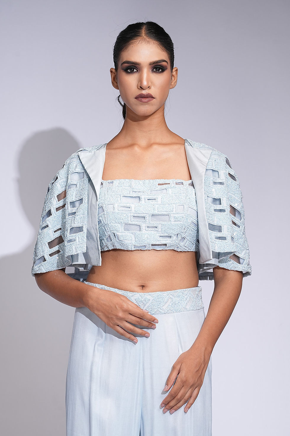 Thumbnail: Model wearing powder blue co-ord pant set with crop top and cape-style embroidered jacket by SHRUTI S – cocktail & event wear