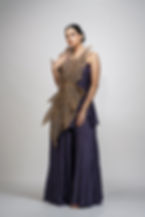 Model wearing a smoked purple one-shoulder sharara set with gold leaf embroidery, posing elegantly