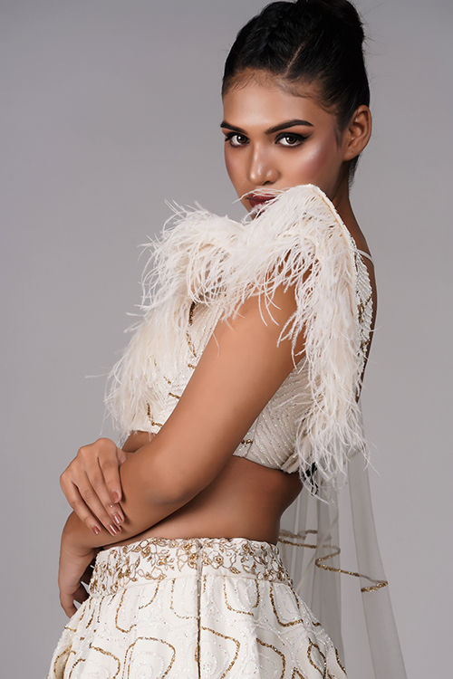 Thumbnail: Close-up of golden thread embroidery and feather trim on off-white blouse