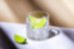 Cut crystal glass with lime wedges on a white surface, lit by bright sunlight with a lone lime wedge in front.