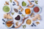 Colorful spices and ingredients on a white background: turmeric, ginger, cinnamon, chia seeds, blueberries, and nuts in various bowls.