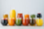 Assorted colorful juices in glasses and pitchers on a gray surface with a plain background. No visible text. Bright and fresh vibe.