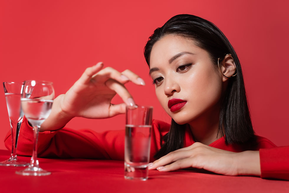 Woman in red gazes pensively at a glass of water on a red table. Red background enhances the scene's dramatic mood.