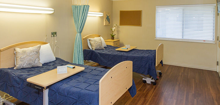 Patient room with two beds, medical equipment, and window blinds