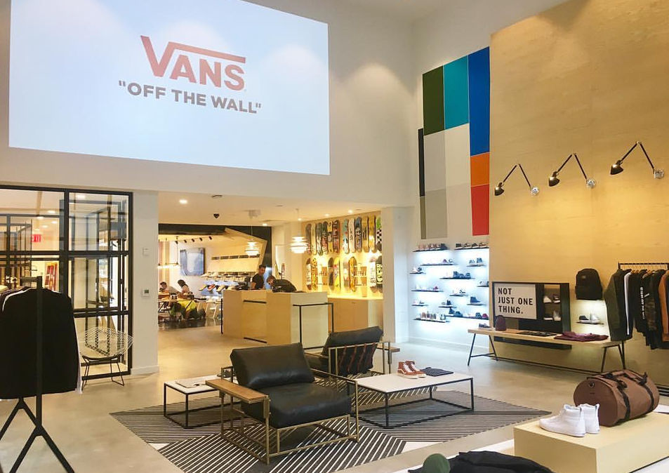 Interior of The General by Vans showing custom shoe displays, apparel racks, and seating areas arranged on clean concrete flooring with wood wall accents.