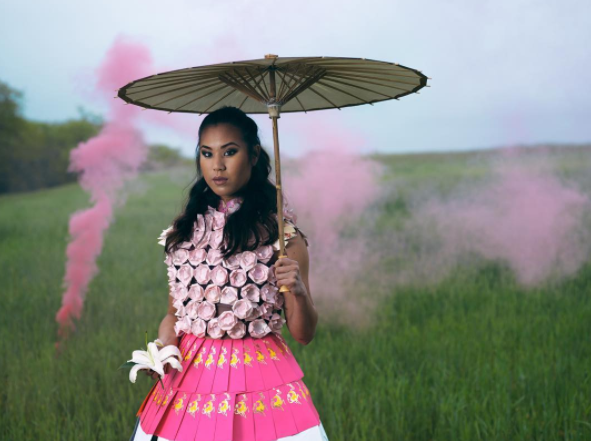 Photo of a girl holding a paper parasol wearing an pink origami and pink envelope hand-crafted dress holding a flower with pink smoke in the background