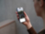 iPhone mockup held in a woman’s hand showing a mobile website layout.