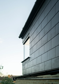 A contemporary building with a black slate roof and a rectangular window with a metal frame. The wall is made of brick.