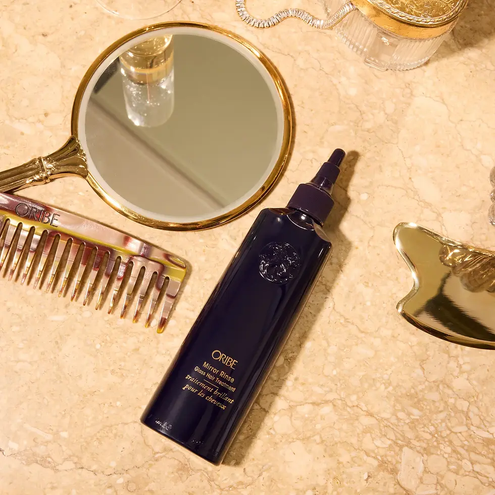 Miniature : "Bouteille de Mirror Rinse ORIBE posée sur une coiffeuse avec un peigne et un miroir, disponible au salon de coiffure Jouvanceau à Lyon 6ème. Ce traitement innovant apporte une brillance éclatante et protège les cheveux tout en facilitant le coiffage."