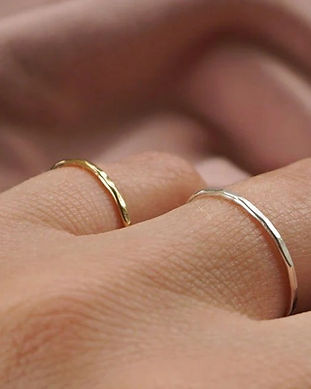 Light pink cloth in background with hand resting on top, wearing two fine ring bands