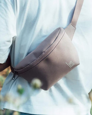 Back of person wearing light blue shirt wearing a grey crossbody bag, with blurred wildflower in bottom left corner