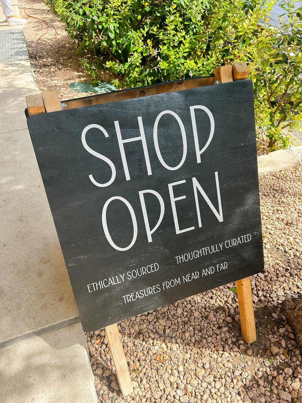 A front shop sign saying shop open, for ethically sourced, thoughtfully curated goods and handmade treasures from around the world, an invitation to shop local, sustainable and ethical, supporting small businesses and craftsmanship