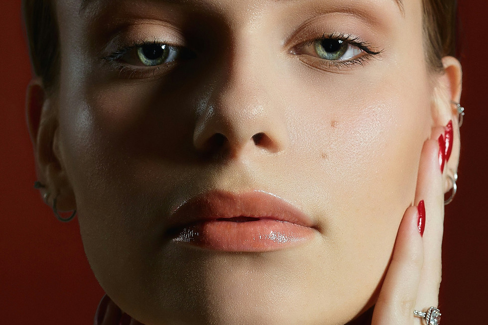 Close-up portrait of a woman with red nails and jewelry touching her face.
