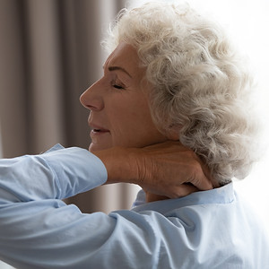 Tired senior grandma rubbing stiff neck suffering from fibromyalgia pain