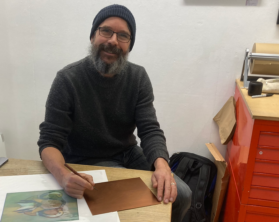 Tim Mitchell smiles in the Greenwich Printmakers gallery, his hand poised with an etching tool over a copper plate