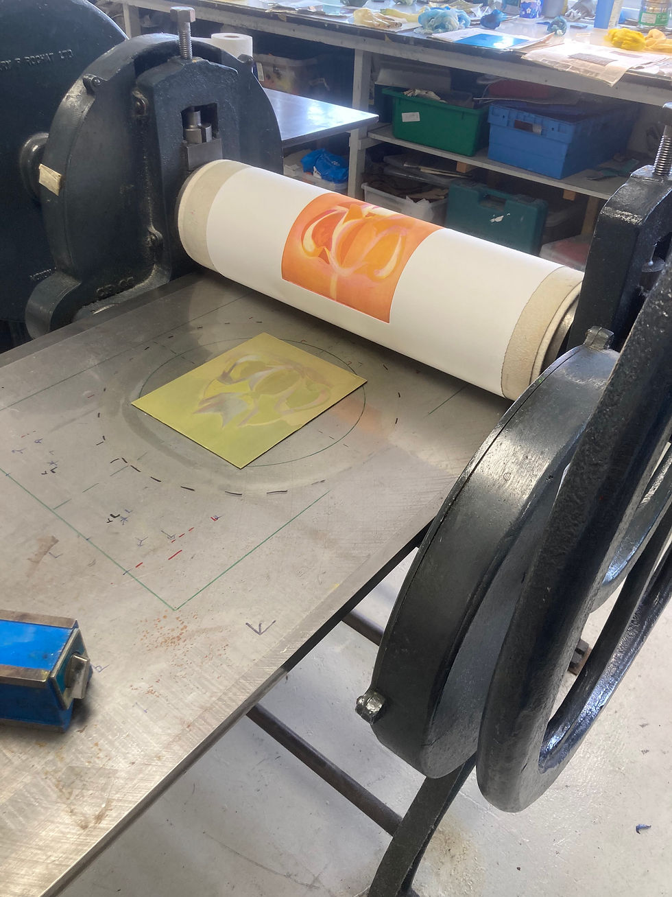 The Mandarin duck print partway through the printing process, with the paper showing orange, pulled back on the etching press, over a yellow plate on the press bed
