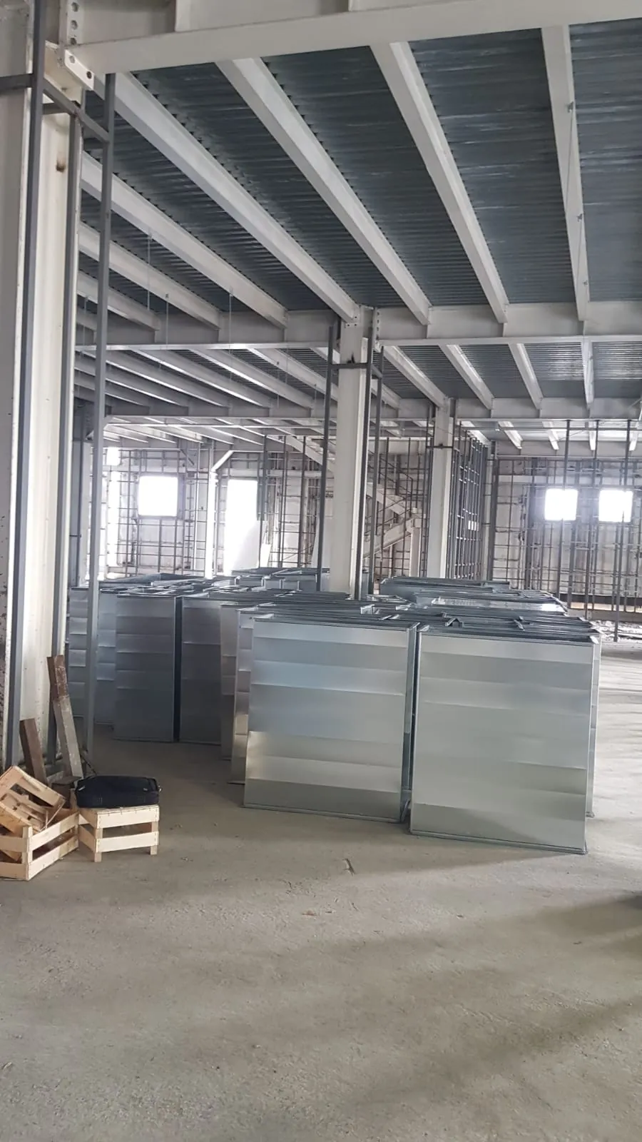 Çelik taşıyıcılı kaba iç mekânda sıralanmış büyük dikdörtgen galvaniz kanal parçaları