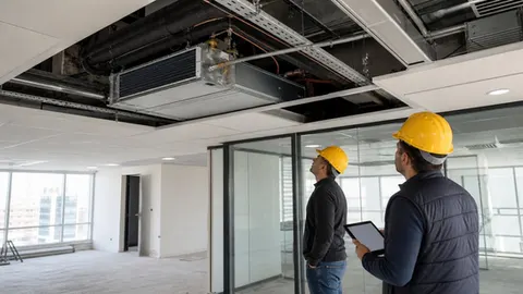Ofis yenilemesinde açık tavandaki fancoil, borulama ve kanalları inceleyen mekanik tesisat mühendisleri.