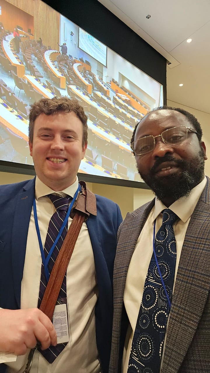 Two men smiling in suits, one holding a gavel