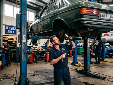 Mechanic working under a car raised on a two-post hoist in a busy automotive workshop