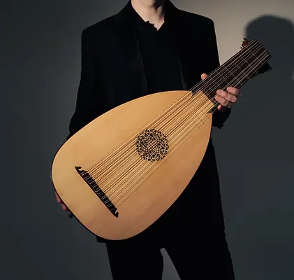 Close up of Toby Carr holding a lute, wearing a black suit