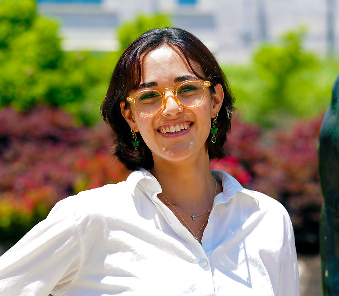 Young woman smiling with yellow glasses and white shirt outdoors.