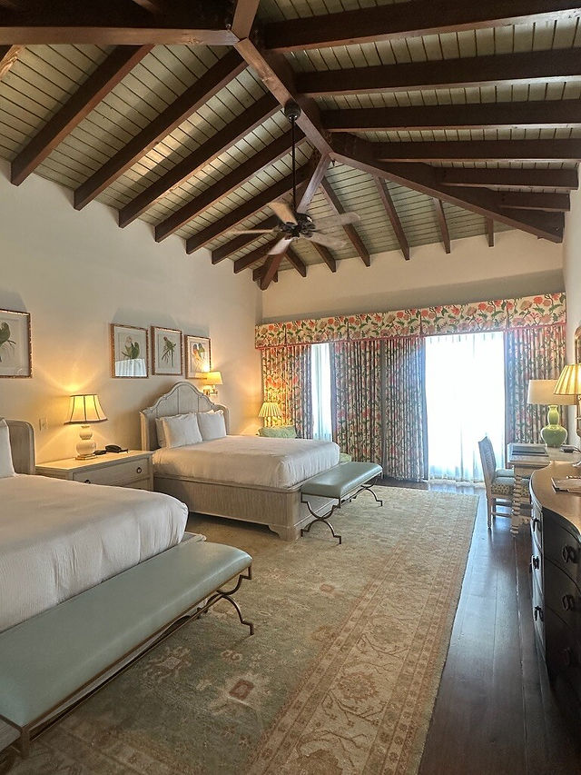 Spacious guest room at Sea Island Resort in Georgia with exposed wood beam ceilings, double beds, and upscale coastal luxury accommodations.