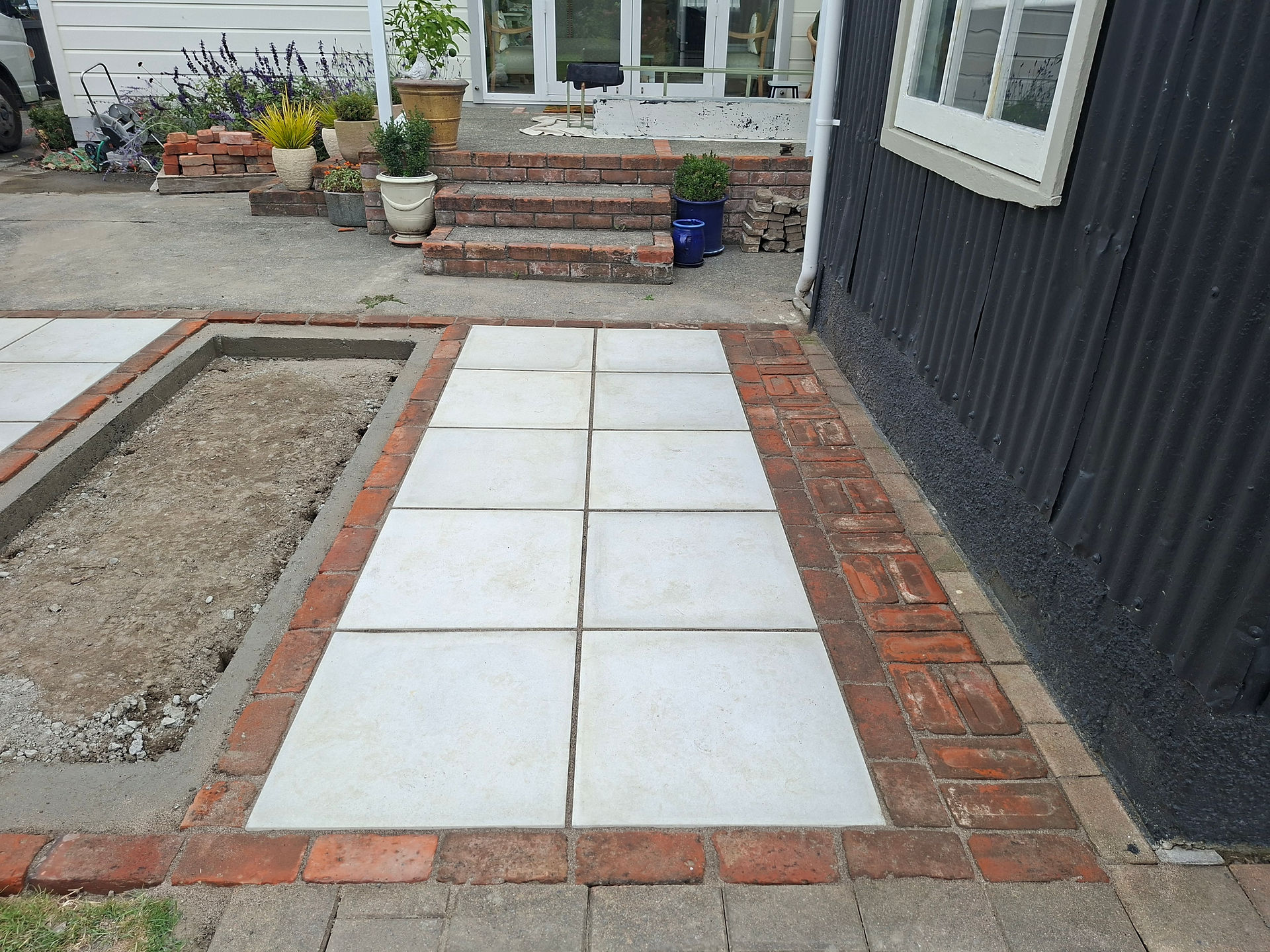 Completed paving area featuring large-format pavers framed with reclaimed brick edging as part of a 