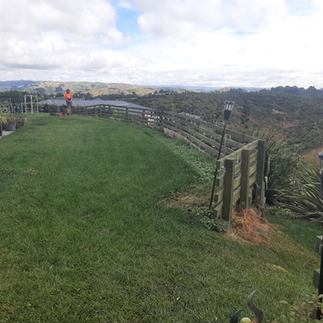 Wide view of hillside lawn showing failing timber retaining wall along edge in Napier