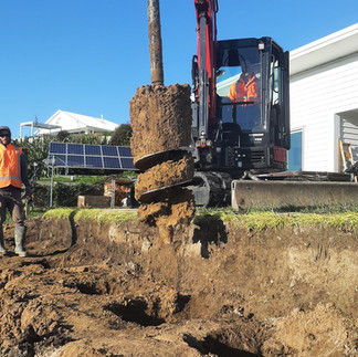 Contractor guiding auger drilling along retaining wall line on sloped site in Napier