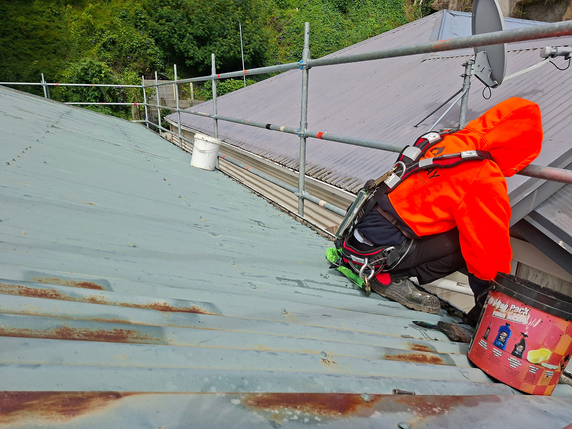 Painter preparing roof surface with safety harness before coating in Napier