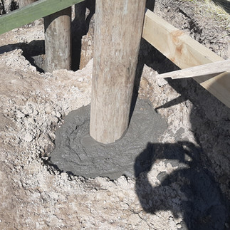 Concrete poured around timber retaining wall post to secure footing in Napier