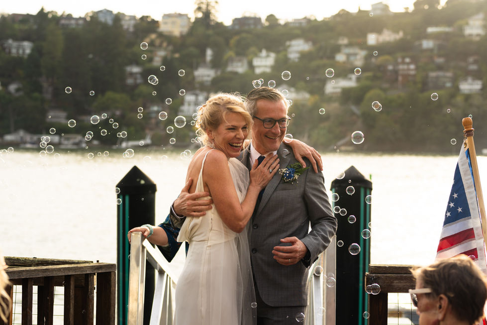a bride and groom are standing on a dock with soap bubbles falling around them