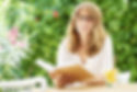 Smiling woman reading a book while seated at a table outdoors
