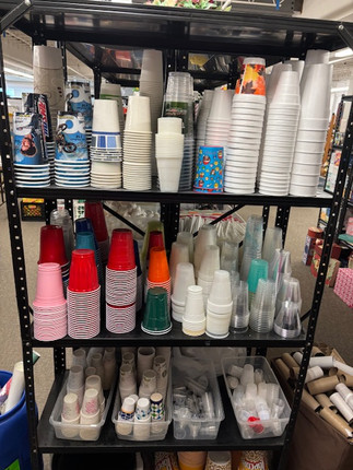 Assorted donated paper, styrofoam and plastic cups displayed on a metal shelf at a creative reuse center