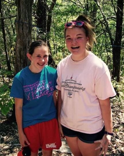 Two girls standing in a wooded area