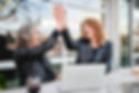 Two older women high-fiving while seated at table outdoors