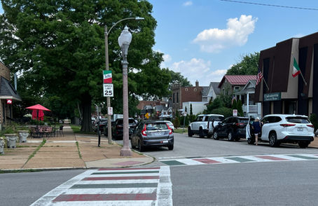 Street view with parked cars, streetlights, a striped crosswalk and American and Italian flags