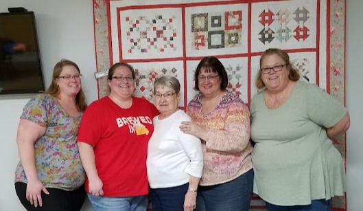 Group of five woman in front of a quilt on the wall