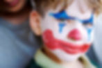 A young child wearing clown makeup on his face