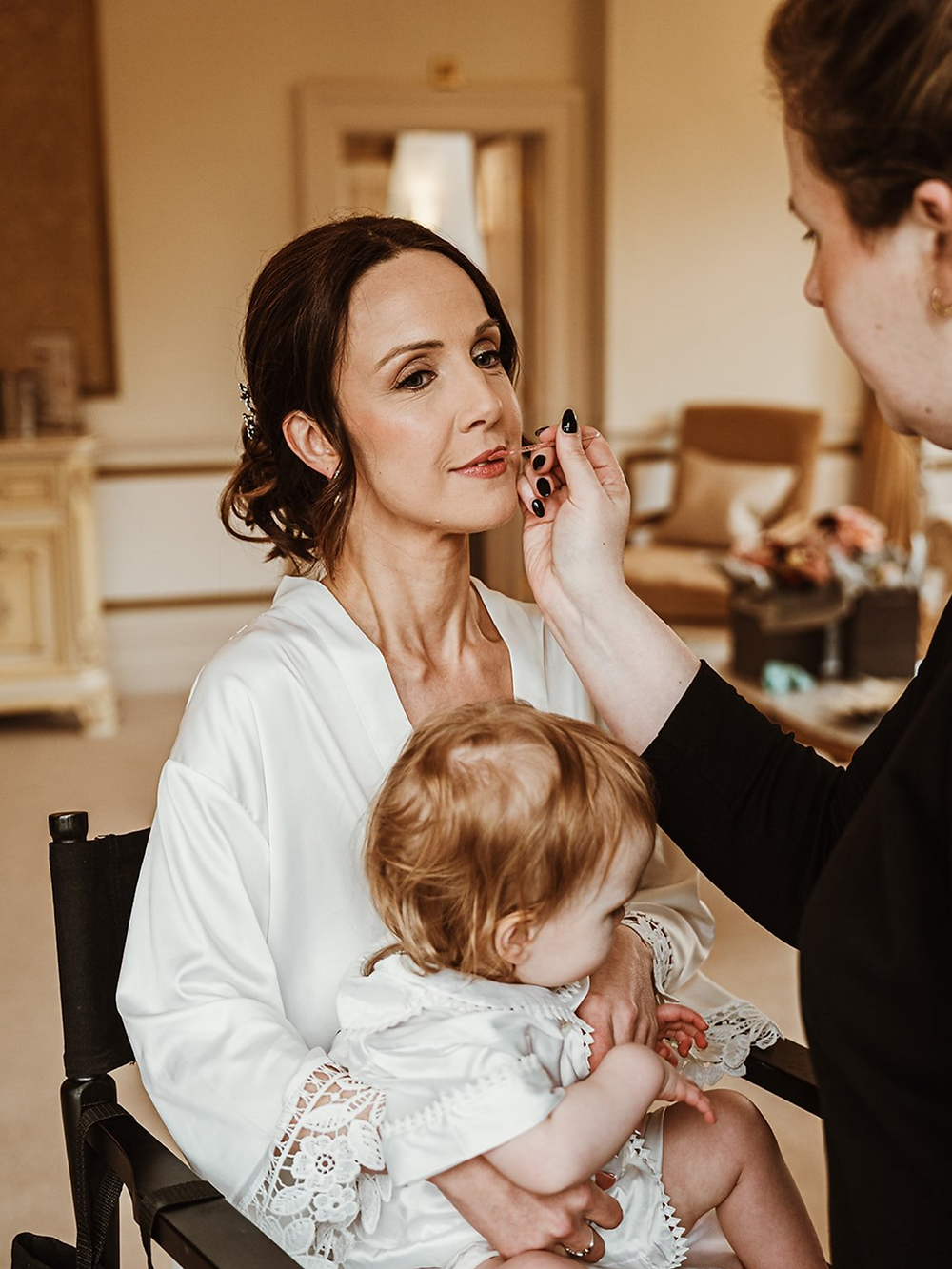 Woman getting bridal make up while holding a baby