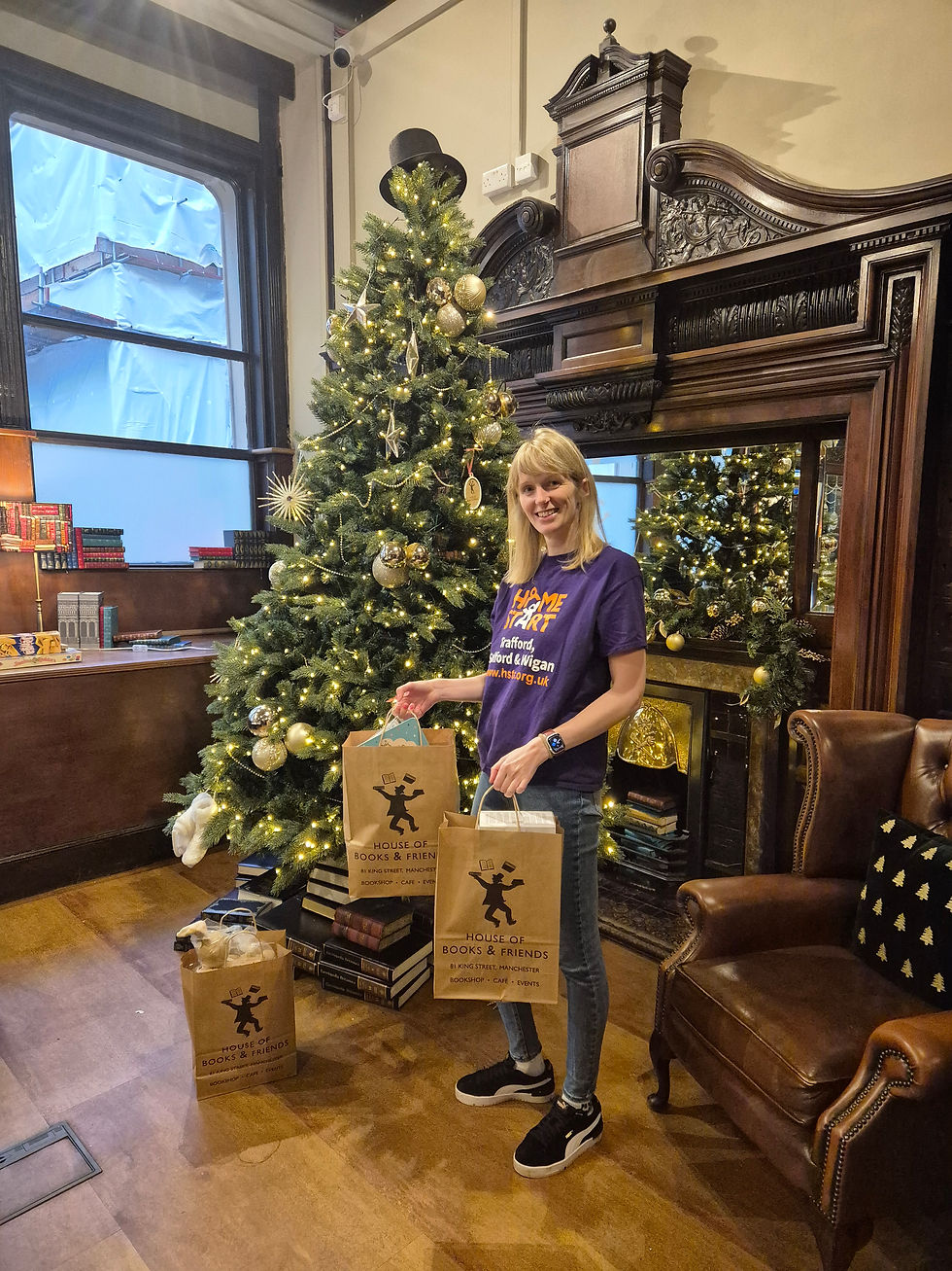 A volunteer wearing a Home Start t-shirt stands by a Christmas tree, holding paper bags with gifts.