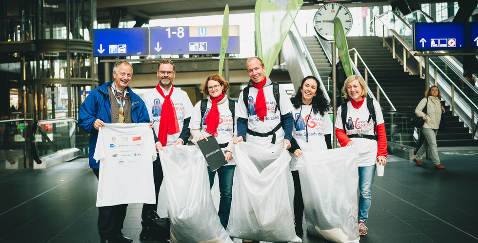 6 people stand in the main station in Berlin, wearing Wrap Up t-shirts and holding collection bags for coats.