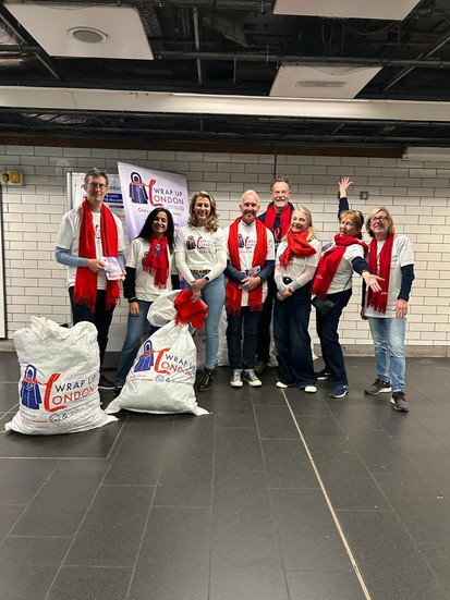 Seven volunteers wearing white branded t-shirts and holding bags with donated coats.